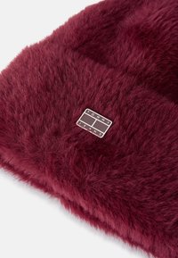 Fular din blană artificială burgundy, cu o textură moale și un patch rectangular argintiu cu eticheta "TOMMY JEANS."