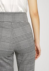 Skräddarsydda rutiga byxor tillverkade av ett strukturerat tyg, med hög midja och en blandning av svart- och vitrutiga mönster.