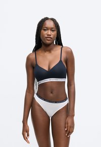 Tmavomodrý bralet s nastaviteľnými ramienkami a bielym pásom s logom "TOMMY HILFIGER"; doplnený o biele bikiny nohavičky s tmavomodrým pásikom.