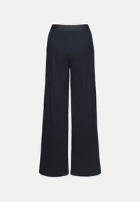 Laiad püksid tumedast sinisest kangast, millel on sile tekstuur. Omab musta elastset vöökohta, millel on 'L'Amand' bränding.