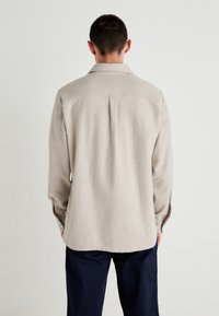 Jasnobeżowa koszula z długim rękawem z kołnierzykiem, zapinanymi mankietami i prostym dołem. Gładka tekstura z subtelnym wzorem tkanym.
