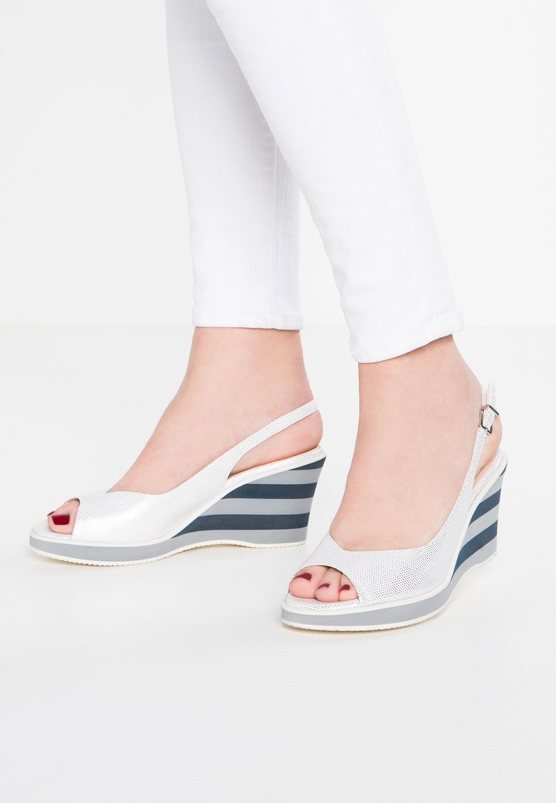 Sandales compensées blanches à bout ouvert, dessus texturé argenté et semelle en caoutchouc rayée bleue. Bride arrière réglable avec détail de boucle.