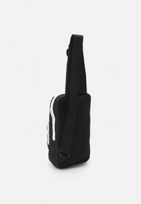 Borsa a tracolla nera realizzata in tessuto testurizzato, con un design a tinta unita e una striscia bianca a contrasto, tracolla regolabile e forma rettangolare compatta.