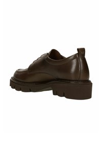 Chaussure en cuir marron avec un bout arrondi, semelle en wedge basse et couture contrastante. Tirette à l'arrière et détail du logo sur le talon.