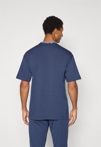 Marineblå bomulds t-shirt med korte ærmer, med en kontrasterende sort og hvid mærke langs kraven. Enkel, afslappet pasform.