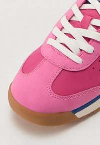 Basket de couleur rose, composée d'un mélange de matériaux synthétiques lisses et de mesh, avec des lacets blancs et une semelle en caoutchouc beige avec des accents bleus.