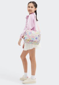 Bolso con estampado floral y acentos en rosa, de forma rectangular, fabricado en tela suave, con correa ajustable y un charm decorativo adjunto a la cremallera.