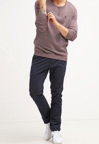 Licht kastanjebruin gebreid sweater met een ronde halslijn en lange mouwen, gecombineerd met marineblauwe slim-fit broek en witte sneakers.