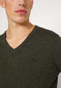 Dunkelgrüner V-Ausschnitt-Pullover aus weichem Strickmaterial, mit einem dezenten Logo auf der Brust und Rippstrick-Details am Ausschnitt und Saum.