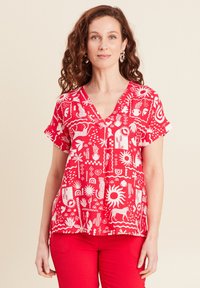 Top rosso a maniche corte con scollo a V e motivi grafici bianchi, inclusi flora, fauna e forme astratte su un tessuto liscio.