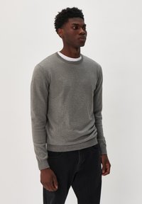 Suéter gris de punto con cuello redondo y mangas largas, que presenta un cuello y puños acanalados, combinado con pantalones oscuros. Diseño minimalista.