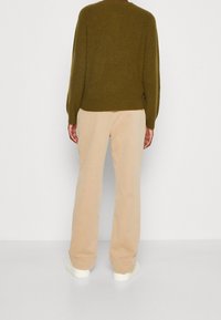 Olivově zelený pletený svetr volného střihu, béžové široké kalhoty a bílé tenisky. Hladká textura, jednoduchý design a žádné viditelné vzory.