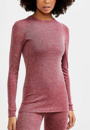 Femme portant un haut à manches longues rouge chiné ajusté et un pantalon assorti sur fond blanc uni.