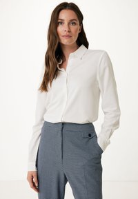 Camicia bianca a maniche lunghe con colletto, abbinata a pantaloni a vita alta a quadri blu e bianchi con tasche laterali.