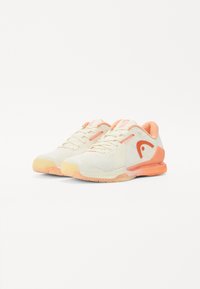 Lightweight athletic shoes in cream and coral. Features a textured mesh upper, rubber sole, and a unique logo accent. Durable and breathable design.