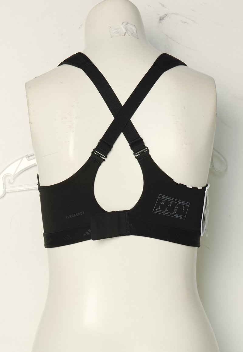Reggiseno sportivo nero con spalline incrociate regolabili, chiusura con gancio, dettaglio perforato e branding Aeroready. Etichetta di cura allegata.