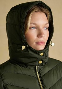 Tmavozelená prešívaná bunda s kapucňou, s prešívaným dizajnom, zlatými kovovými prvkami a zipsom.