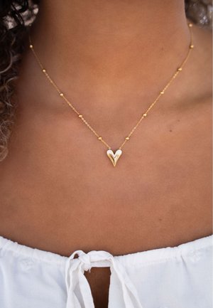 Collana in oro con un piccolo pendente a forma di cuore lucido, caratterizzato da un design a strati, accentuato da piccole perline sferiche lungo la catena.