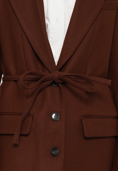 Rjav blazer iz volnenega mešanega materiala z pasom za zavezovanje, enojnim črnim gumbom za zapiranje, izrezanimi ovratniki in dvema sprednjima žepoma. Teksturiran zaključek tkanine.