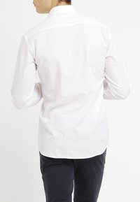 White long-sleeve shirt made of smooth fabric, featuring a standard collar, curved hem, and a clean, minimal design.