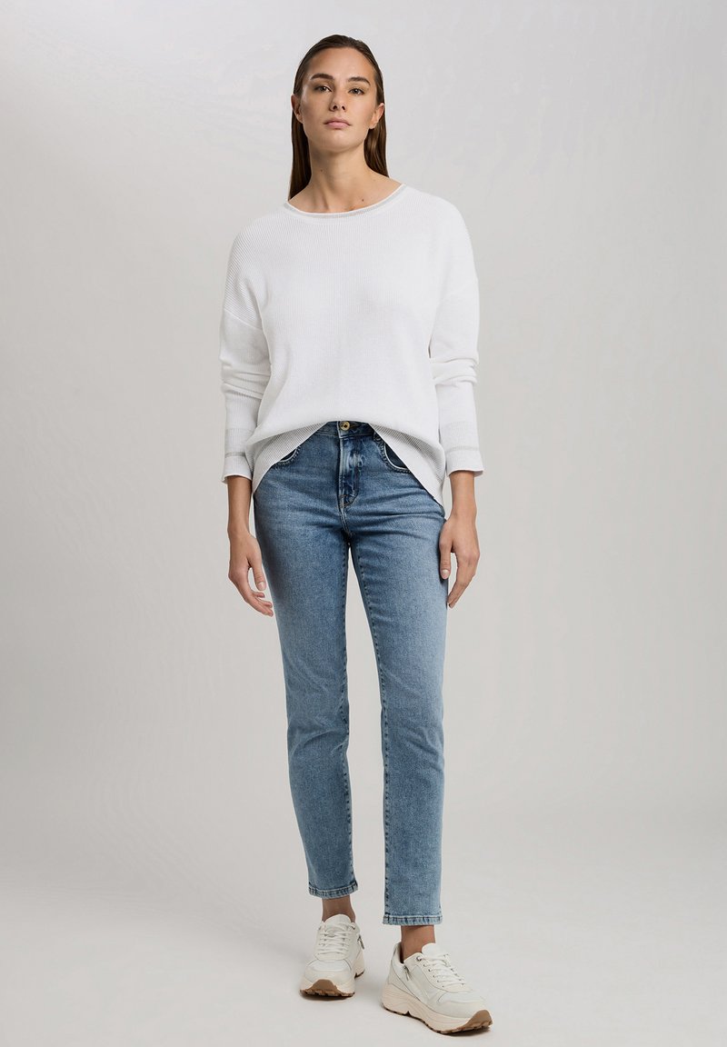 Weißer, gerippter Pullover mit langen Ärmeln, kombiniert mit hellblauen, schmalen Jeans und weißen Sneakers. Lässiges Outfit mit entspannter Passform.