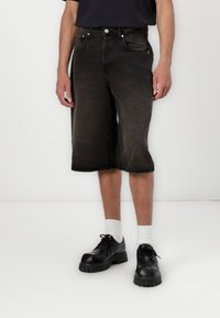 Sorte denim bermuda shorts med en løs pasform, frayed kanter og forlommer, parret med sorte sko og hvide sokker.