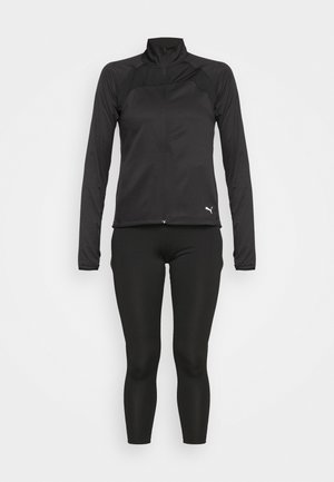 Schwarze Sportjacke mit hohem Kragen und durchgehendem Reißverschluss, kombiniert mit schwarzen enger geschnittenen Leggings. Der Stoff wirkt glatt mit minimalen Akzenten.