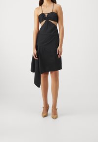 Černé bezrukávové šaty s výřezem a asymetrickým lemem. Vyrobené z hladké tkaniny, s tenkými ramínky a přizpůsobeným střihem.