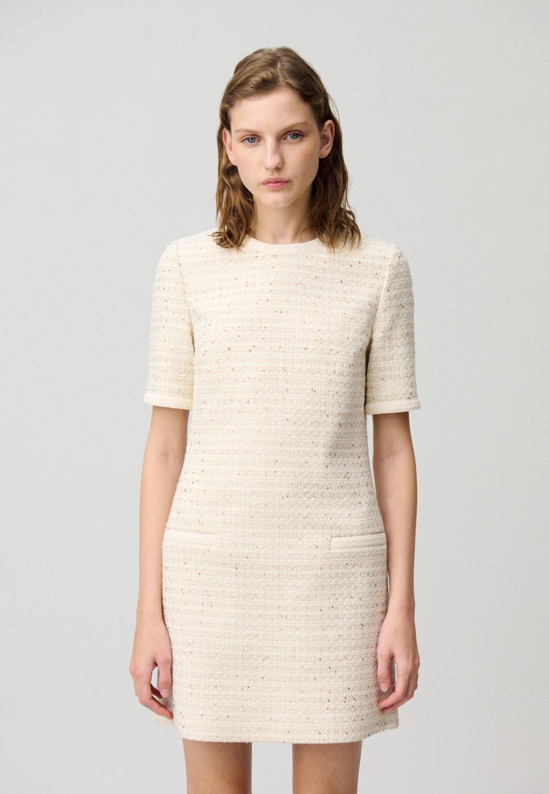 Robe crème à manches courtes en tissu texturé, dotée de deux poches avant et d'une silhouette ajustée, avec un col rond et une coupe au niveau des genoux.