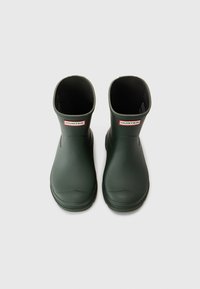 Bottes en caoutchouc vertes avec une finition mate, design court à la cheville, bout arrondi et doublure intérieure, avec un petit logo rouge et blanc.