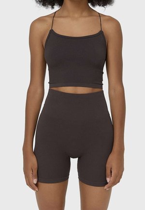 Femme portant un crop top côtelé marron foncé à fines bretelles et un short ajusté taille haute assorti sur un fond neutre.