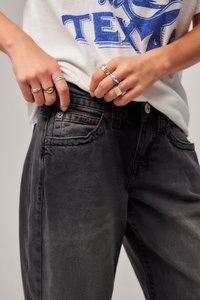 Svart denimjeans med en svakt falmet finish, har fem lommer, sølvfarget tilbehør, og et merkepute på frontlommen.