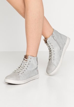 Jasnoszare sneakersy za kostkę z bocznym zamkiem błyskawicznym, sznurowadłami i białą podeszwą, noszone na skrzyżowanych nogach na jednolitym tle.