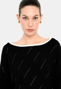 Maglione nero con scollatura a barca bianca, caratterizzato da un motivo testurizzato di punti diagonali argentati e una vestibilità rilassata.
