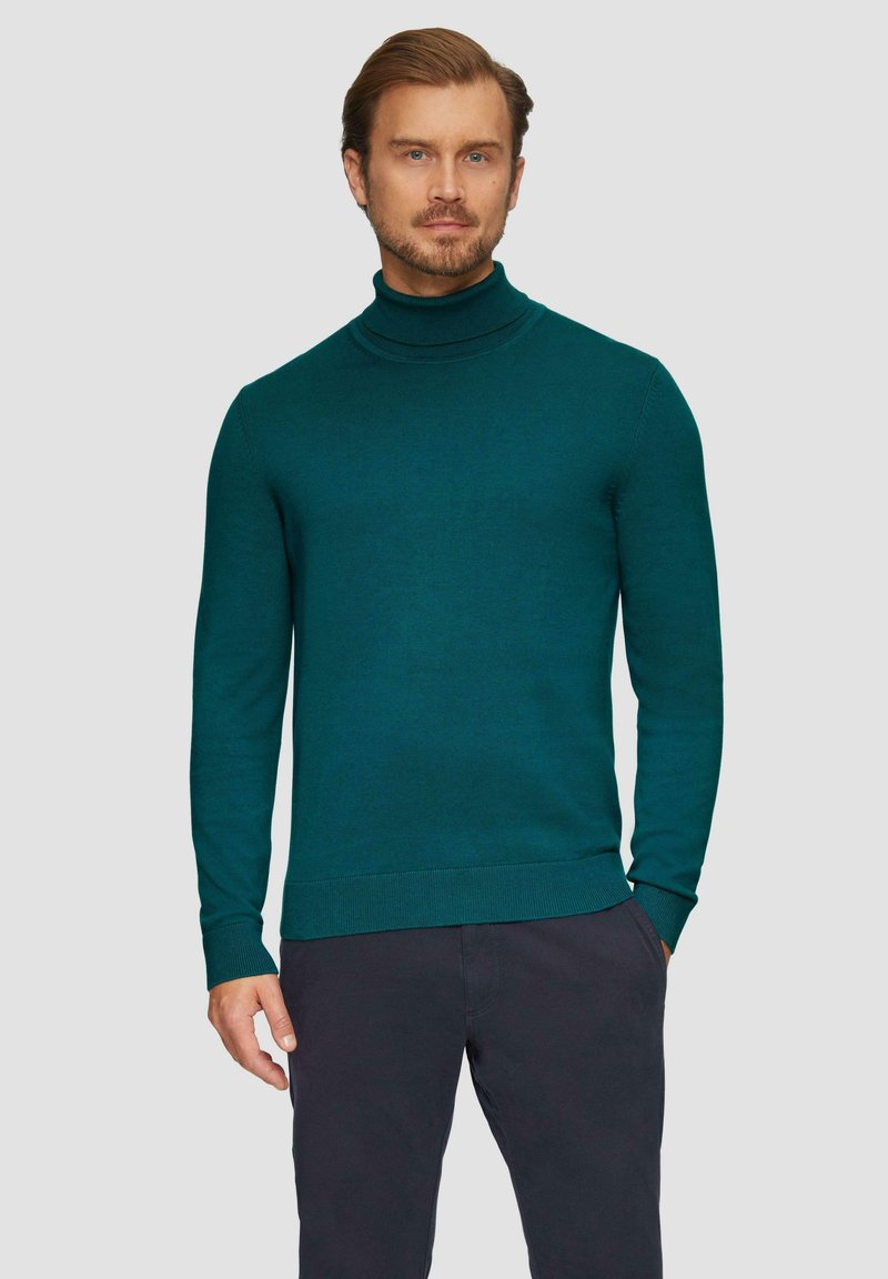 Teal coltrui van een gladde, gebreide stof met lange mouwen en ribgebreide manchetten en zoom, gedragen over donkere broeken.