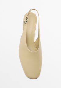Scarpa slingback beige con punta chiusa, texture in pelle liscia e una fibbia argentata decorativa sul cinturino. Suola piatta.