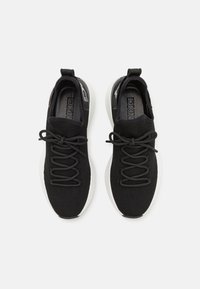 Sneaker neri in maglia con una parte superiore testurizzata, dotati di lacci neri, una suola in gomma bianca e un elastico sul tallone per facilitare l'indossamento.