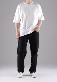 Bílá oversized tričko s kulatým výstřihem, kombinované s černými volnými džíny s kontrastním šitím a bílými teniskami.