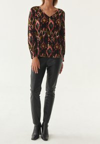 Haut noir à manches longues avec des motifs géométriques colorés, associé à un pantalon en cuir noir ajusté et à des bottes à talons aiguilles.