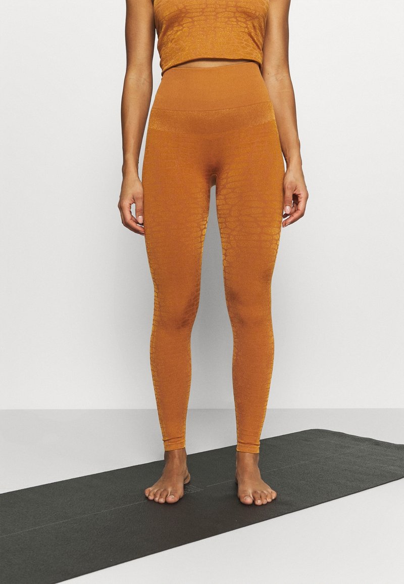 Bursztynowe legginsy z teksturowanym wzorem, wysoki stan, oraz dopasowany krótki top. Minimalistyczna prezentacja na czarnej macie do jogi.