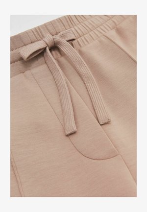 Šviesiai rudos spalvos sportinės kelnės su elastine juosta ir raišteliu, lygiu paviršiumi ir šoninėmis kišenėmis.