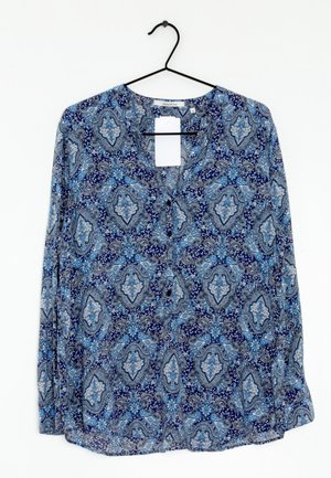 Blouse met lange mouwen en blauw-wit paisleypatroon, hangend aan een zwarte hanger tegen een witte achtergrond.