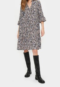 Blommönstrad klänning med trekvartslånga ärmar, V-ringning och veckad nederkant i svarta, rosa och blå nyanser, tillsammans med knähöga svarta läderstövlar.