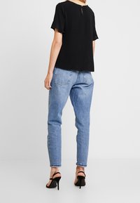 Svart kortärmad topp med en nyckelhålsdetalj bak, matchad med ljusblå högmidjade jeans och svarta klacksandaler.