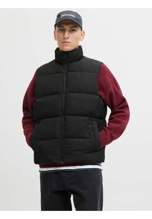 Zwarte puffer vest met hoge kraag, ritssluiting en twee zijzakken, gelaagd over een bordeauxrode wollen trui met geribbelde mouwen.