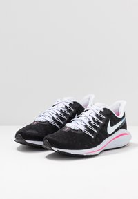 Scarpe da ginnastica nere con una tomaia testurizzata, lacci bianchi e un accento rosa sulla suola. Presentano il logo Nike swoosh bianco.