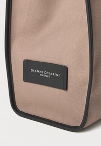 Medium tote bag i lys beige stoff med en teksturert finish. Har svart trim og et rektangulært logo-merke med hvit skrift.