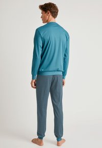 Heren pyjama set met een effen teal lange mouwen top en gestreepte blauwe broek met kleine lichte stippen, elastische manchetten en een relaxte pasvorm.