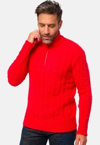 Roter Kabelstrickpullover mit hohem Kragen und halbem Reißverschluss. Mit gerippten Bündchen und Saum, aus einer strukturierten, warmen Wollmischung.
