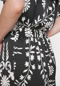 Czarny materiałowy strój z białym kwiatowym wzorem. Posiada elastyczną talię z marszczeniami, zapewniającą luźne dopasowanie i swobodny układ.